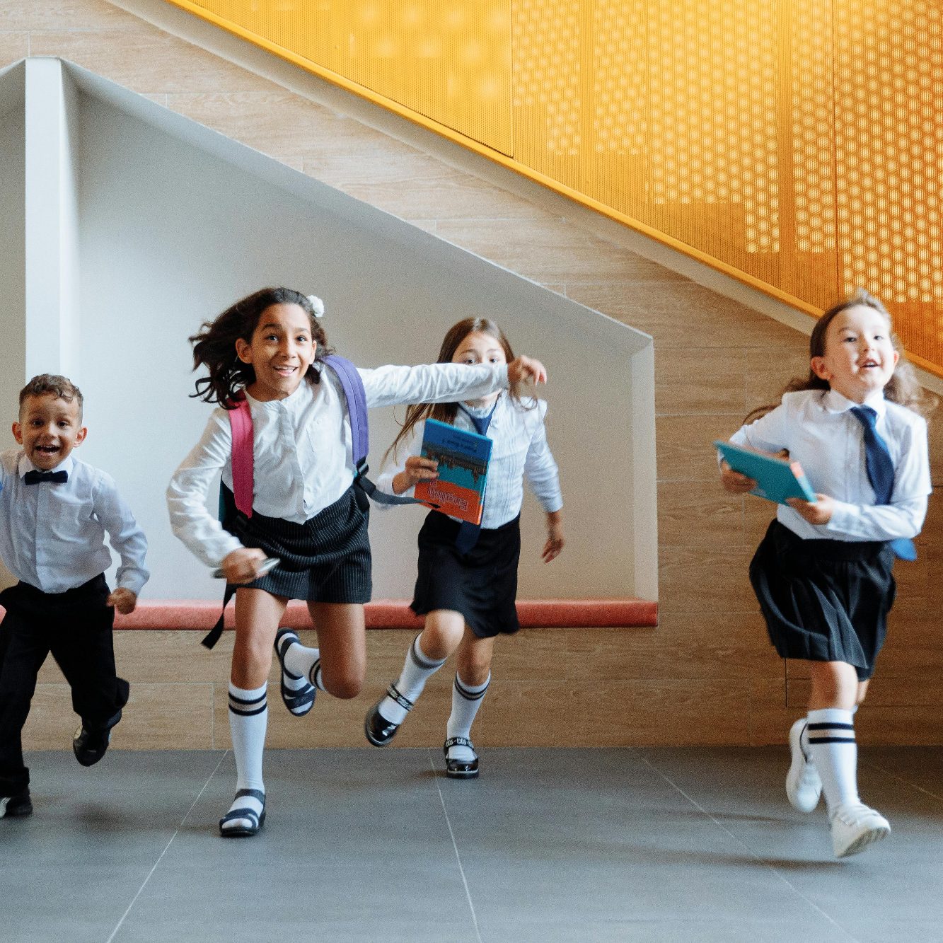 School Children Running Four children in school uniforms joyfully running up towards camera, holding books.